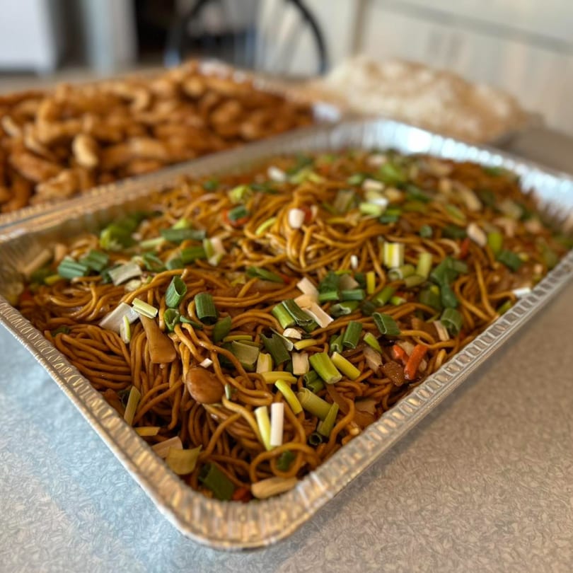 A large aluminum tray of Crystal Garden's lo mein noodles topped with chopped green onions.