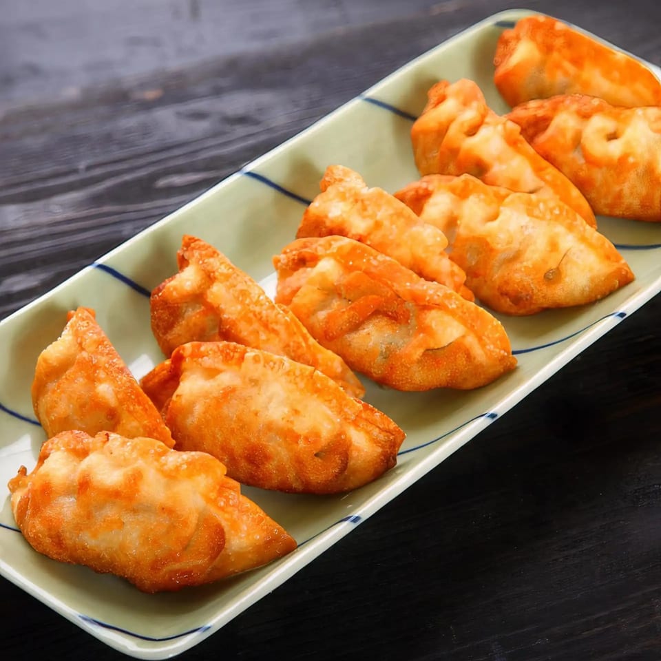 A long, light green rectangular plate filled with golden-brown fried Crystal Garden dumplings on a dark wooden table.