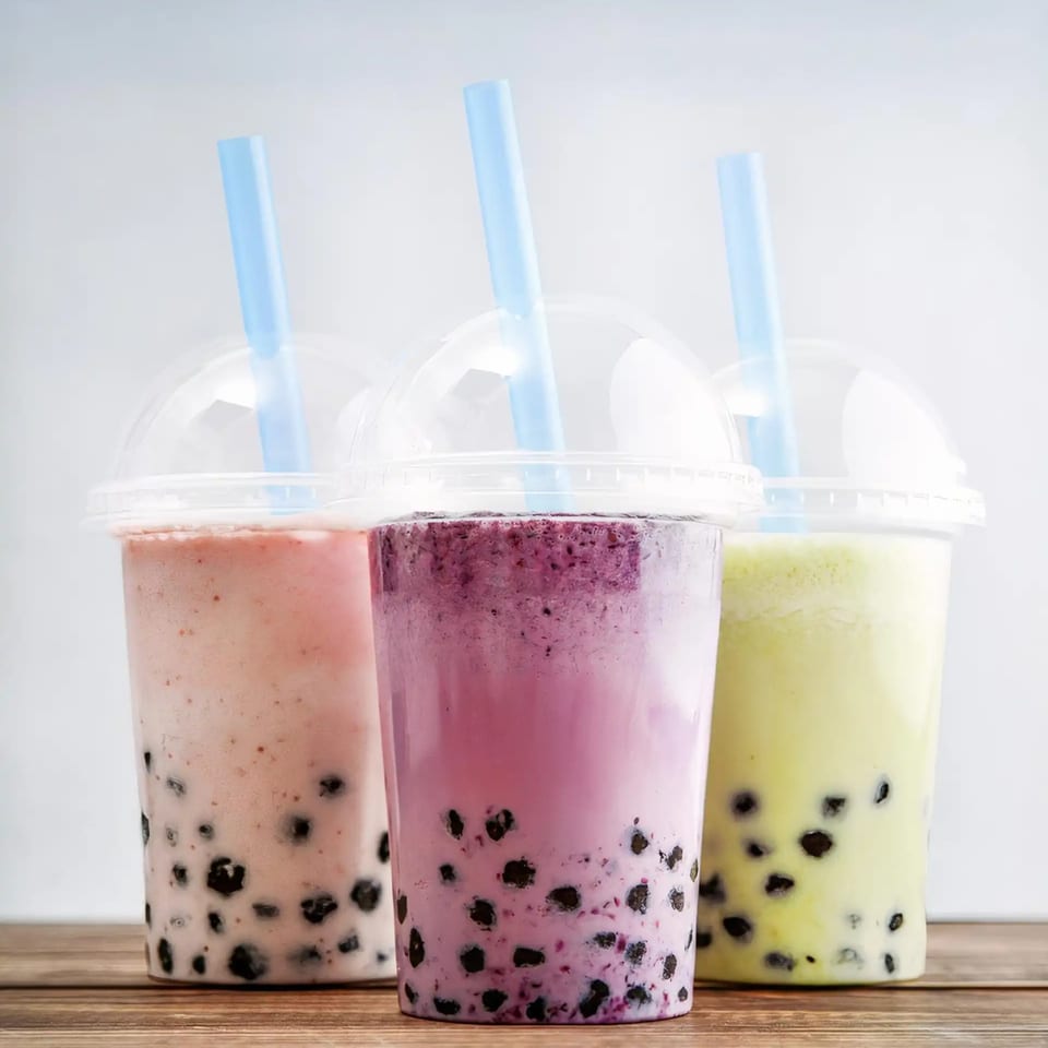 Three colorful bubble tea drinks with tapioca pearls and blue straws on a wooden surface.