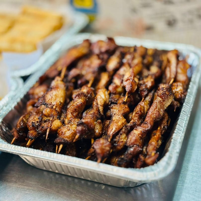 Close-up of numerous dark, glazed chicken skewers in a silver foil tray, ready to serve.
