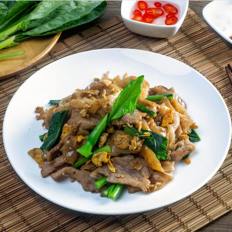 Crystal Garden's stir-fried noodles with beef, green vegetables, and crispy garlic on a white plate.