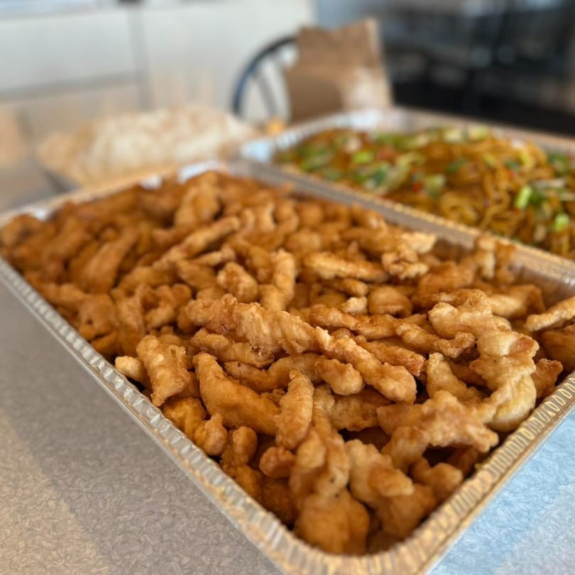 Two catering trays of Crystal Garden's Asian-fusion food, featuring crispy fried chicken and lo mein.